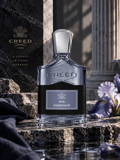 Creed Iris Debonair Eau de Parfum bottle in a luxurious stone setting with purple iris flowers, classical columns and cool blue-grey styling