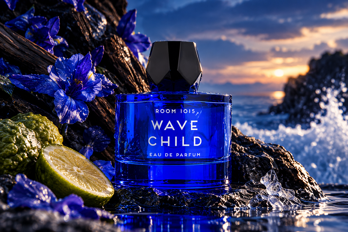 Room 1015 Wavechild Eau de Parfum unisex fragrance bottle in vibrant cobalt blue glass with black geometric cap, surrounded by blue flowers, citrus fruit and ocean waves at sunset